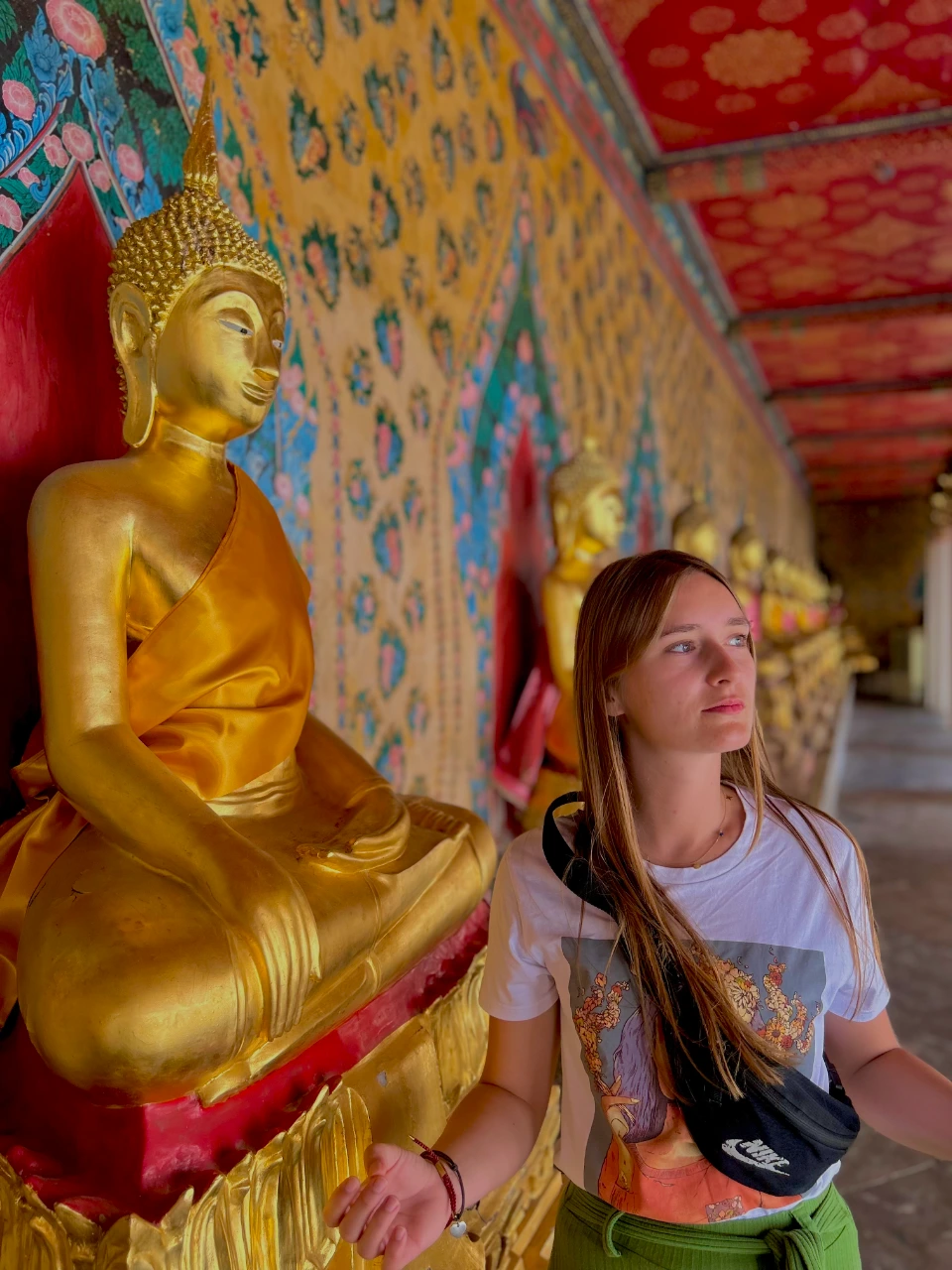 Wat Arun świątynia w Bangkoku, kobieta stoi obok złotego posądu Buddy